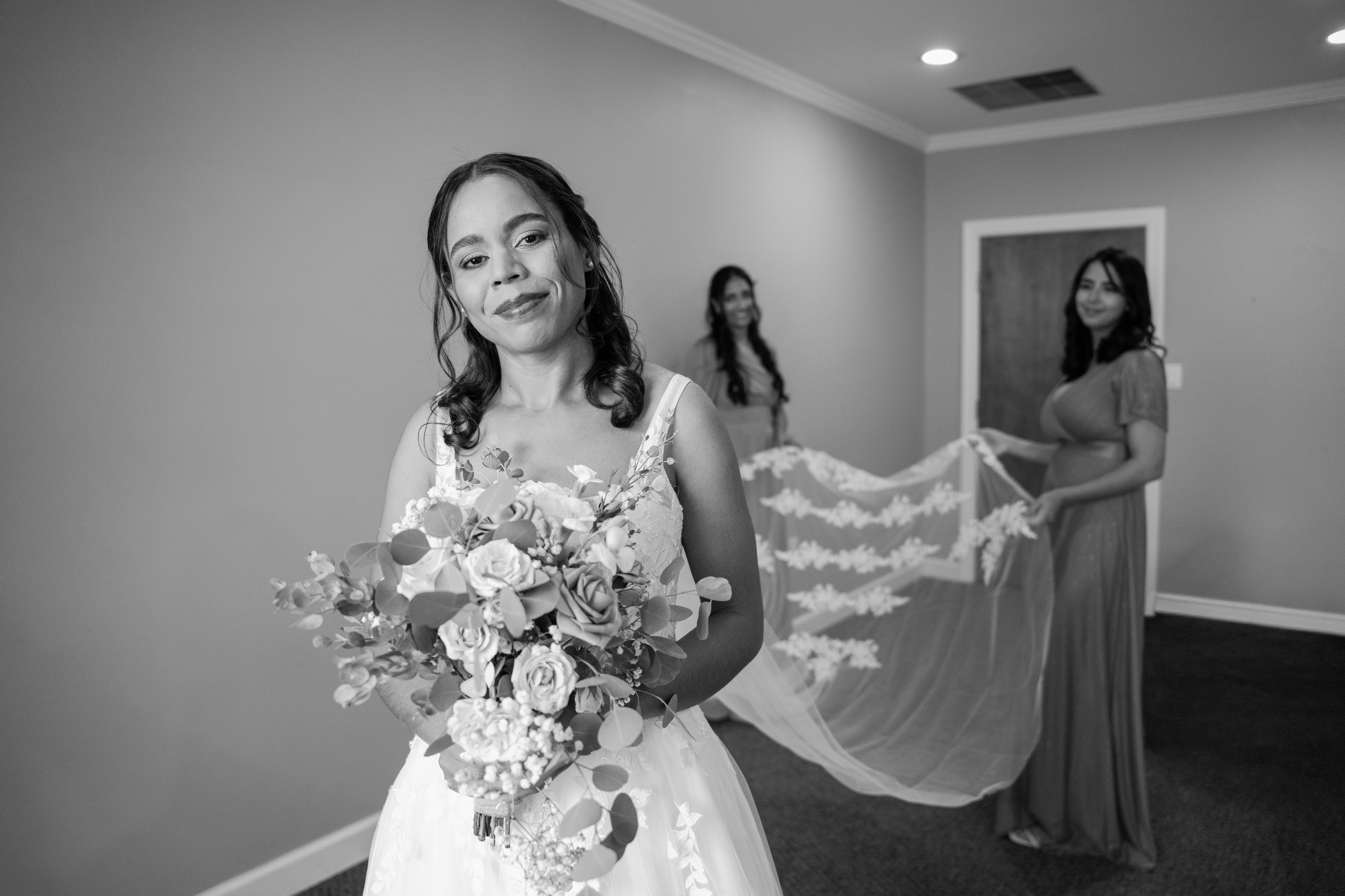Bride holding bouquet with bridesmaids holding her veil