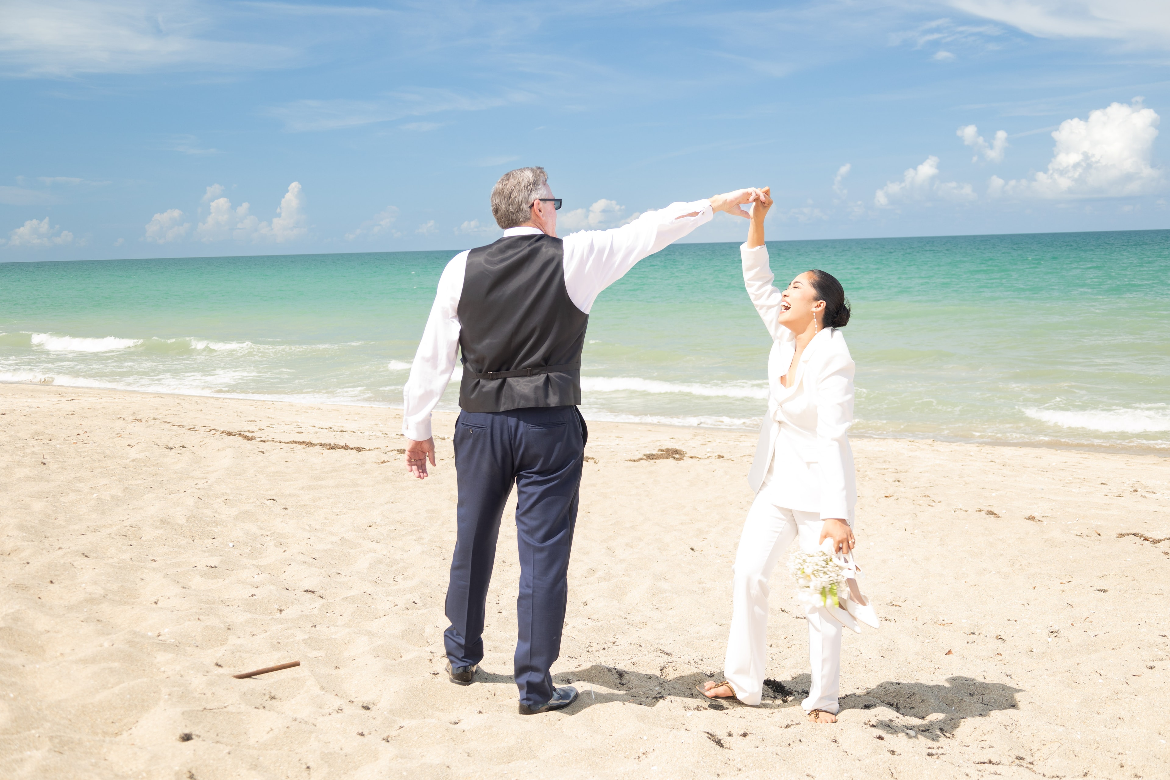 Couple dancing on the beach, bride twirling in white suit