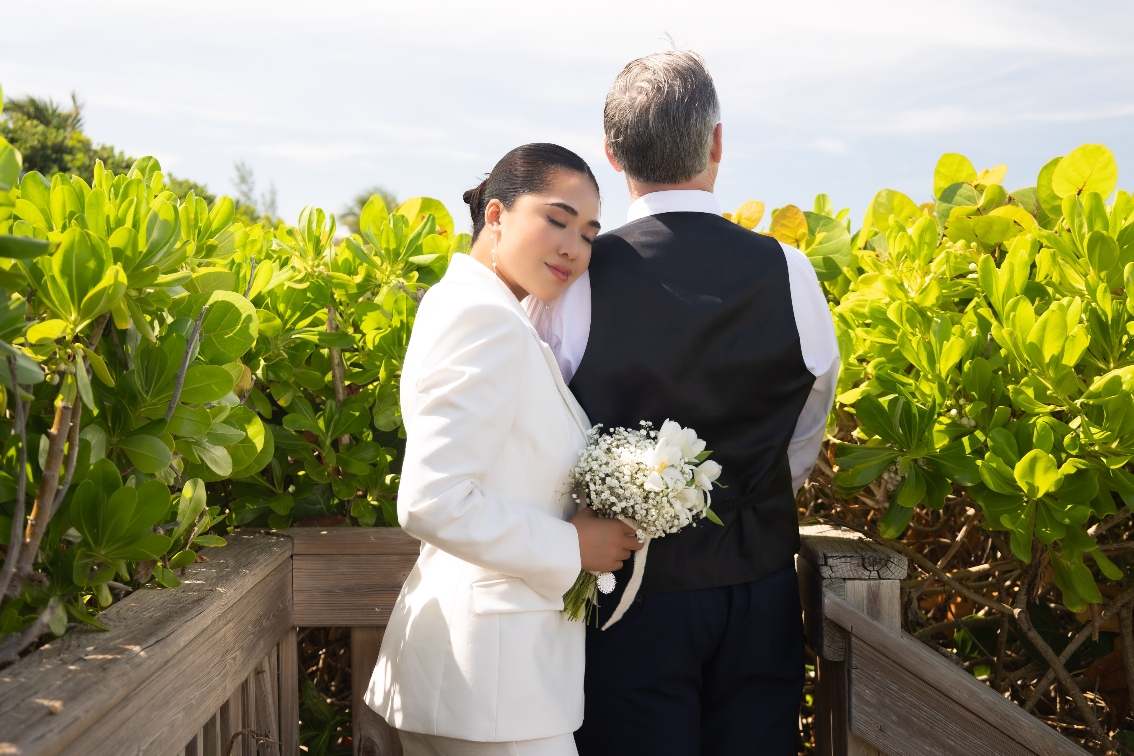 Bride resting head on groom's shoulder on tropical boardwalk