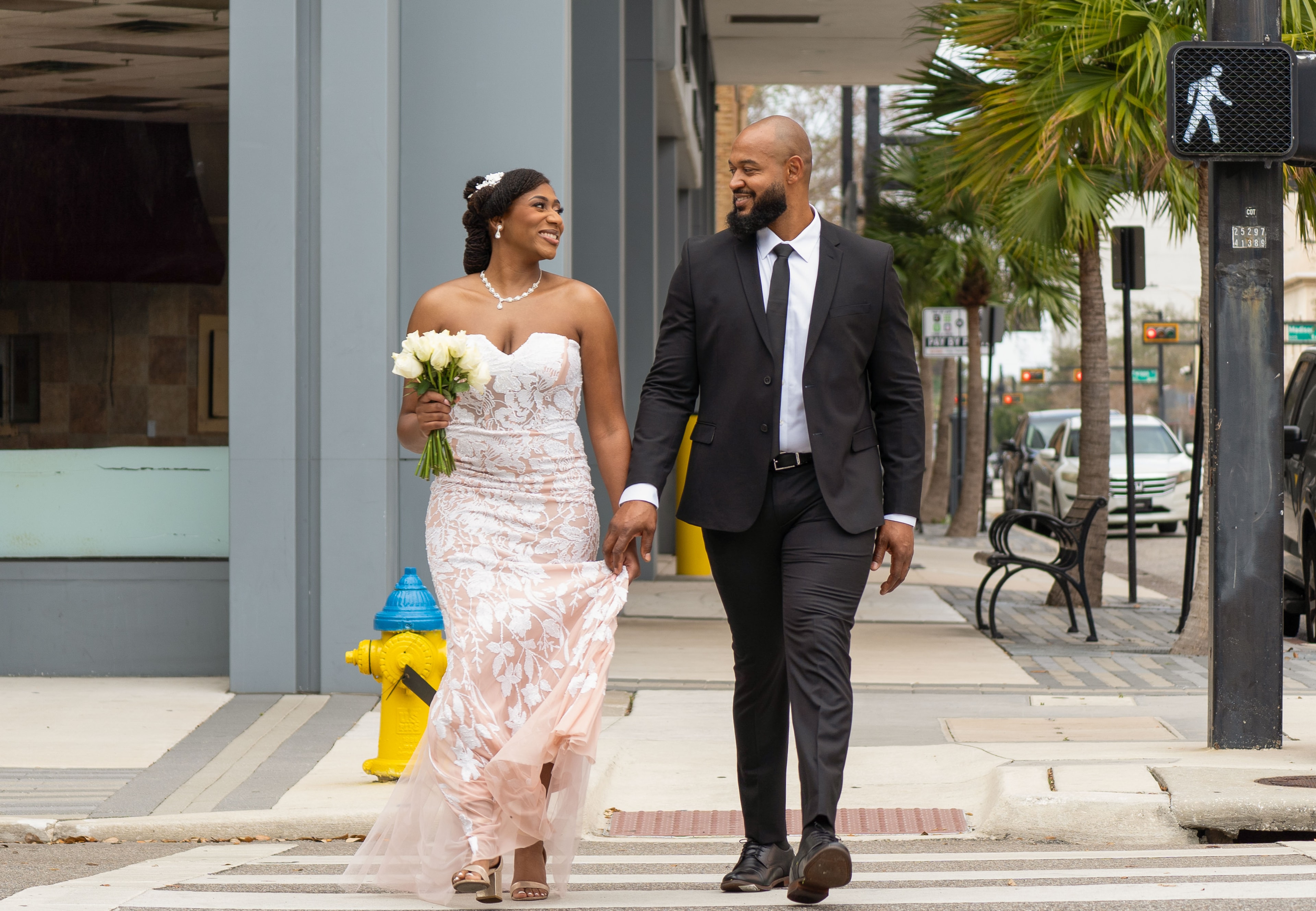 Bride and groom walking hand-in-hand across a crosswalk, bouquet in hand