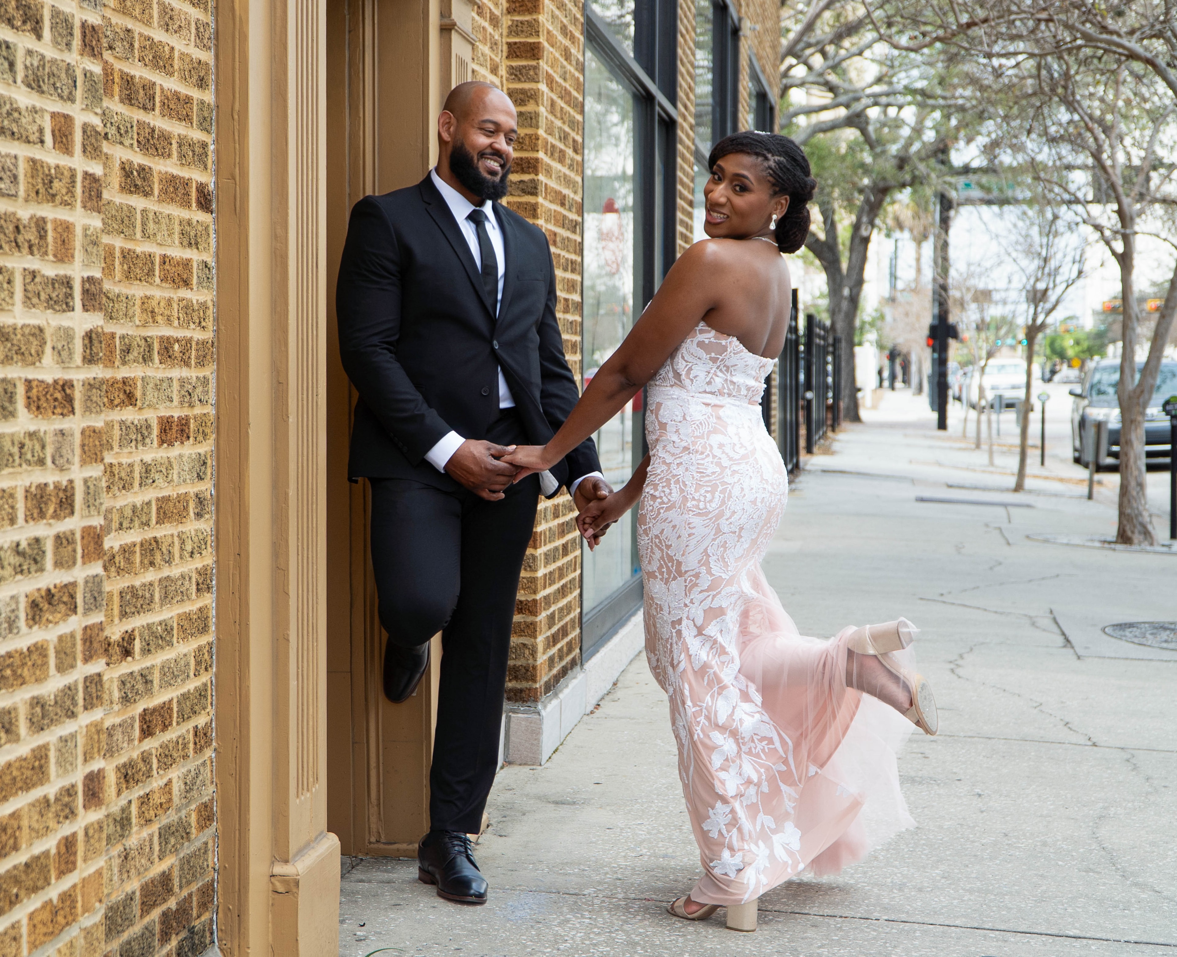 Couple holding hands walking down an urban street, bride glancing back over her shoulder