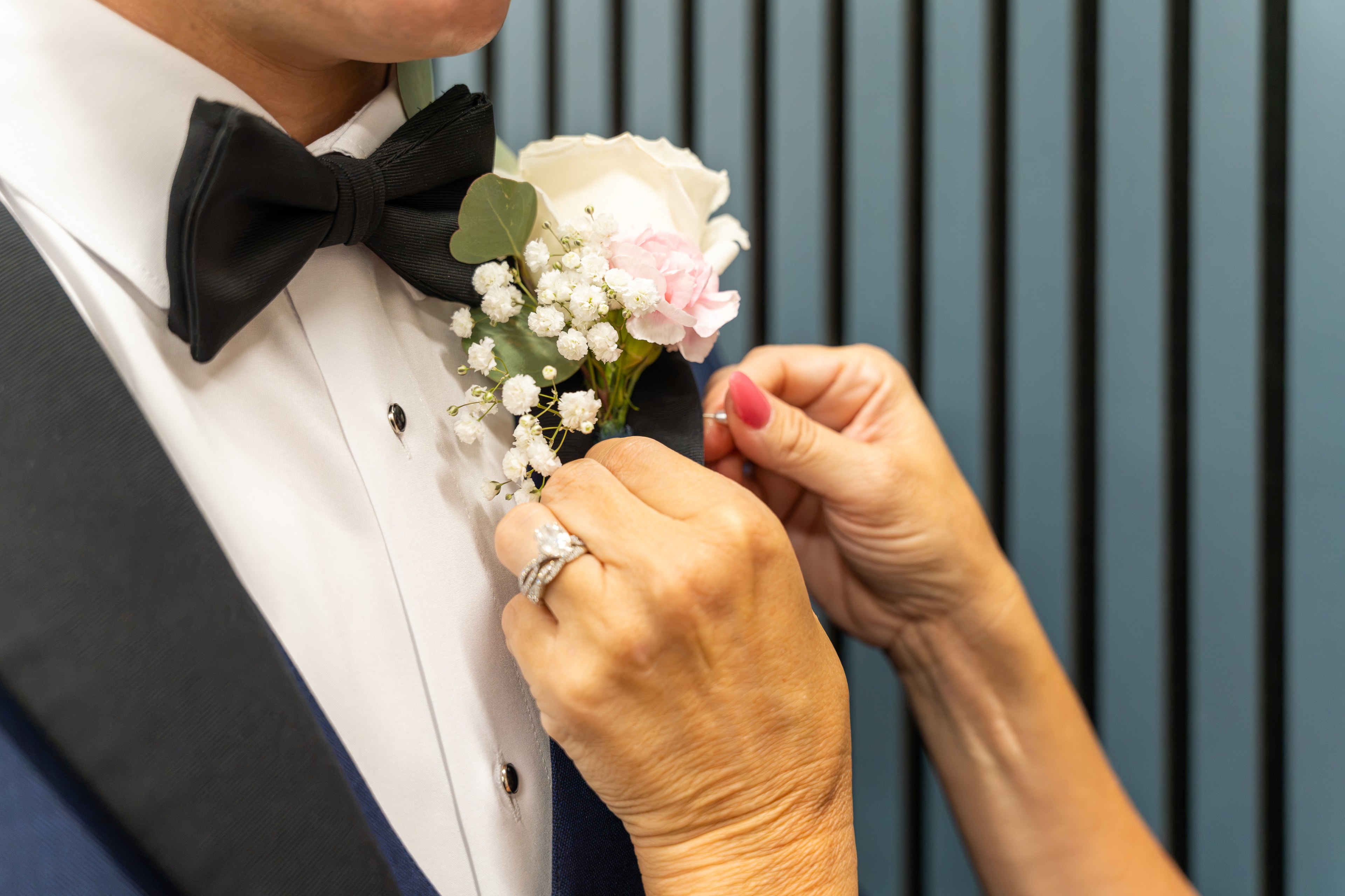 Close detail of boutonniere being pinned on groom's lapel