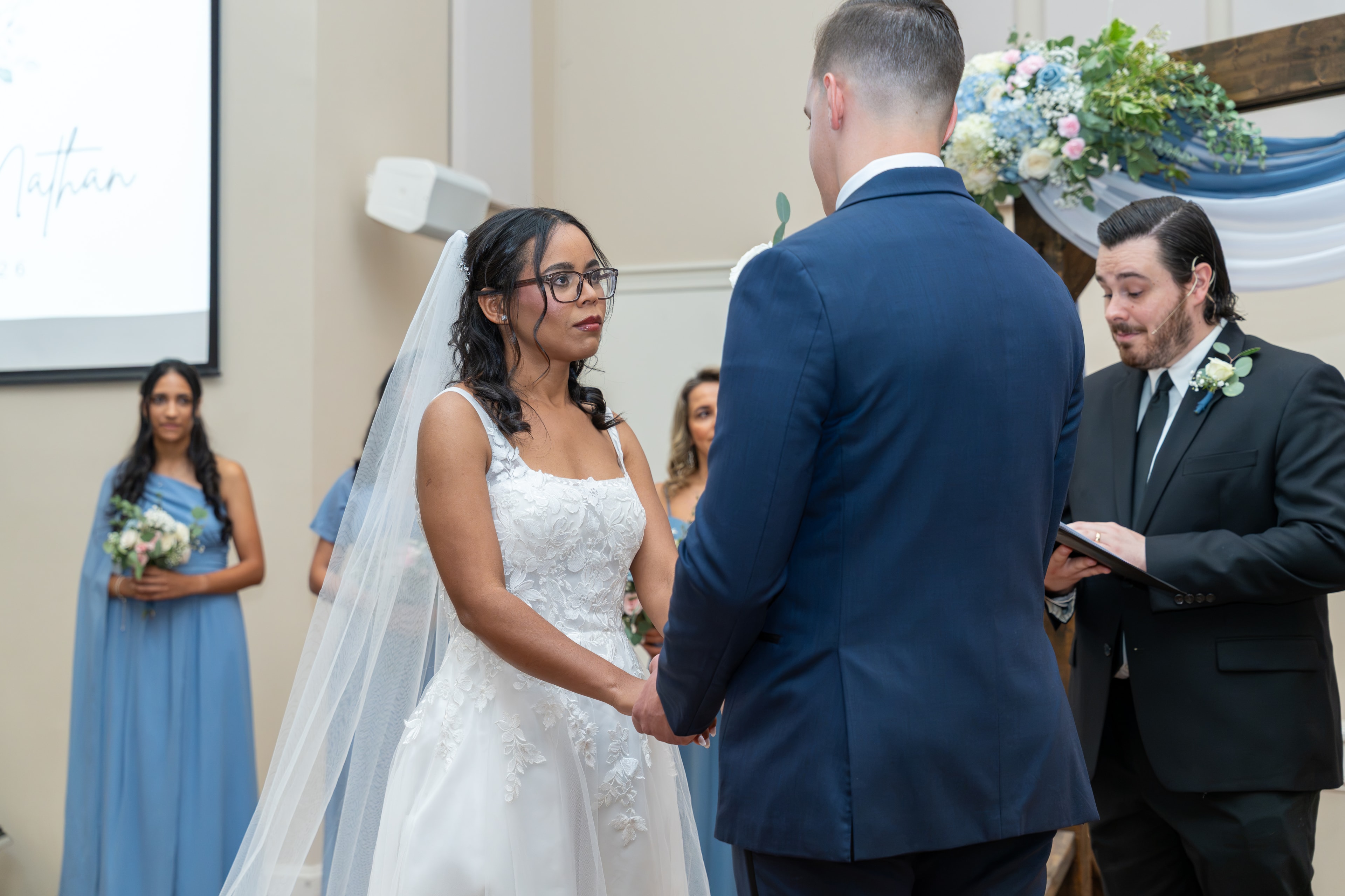 Bride and groom exchanging vows at the altar surrounded by blue florals
